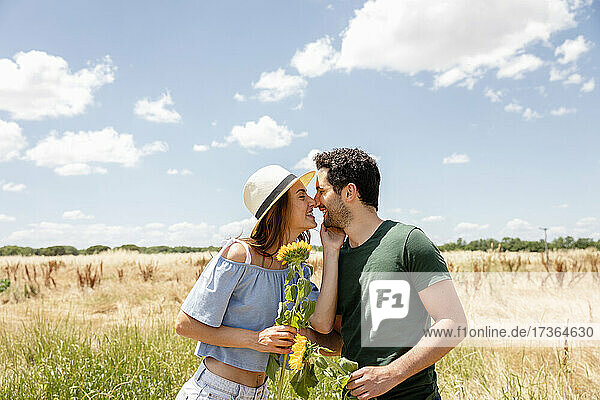 Smiling couple with sunflowers rubbing noses during sunny day