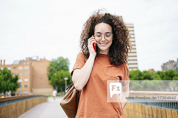 Schöne  lächelnde  lockige Frau mit Brille  die mit einem Mobiltelefon spricht