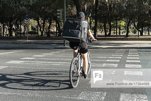 Junge Lieferfrau mit Rucksack auf dem Fahrrad auf der Straße an einem sonnigen Tag