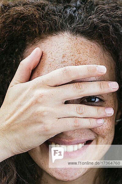 Lächelnde junge Frau  die ihr Auge mit der Hand bedeckt
