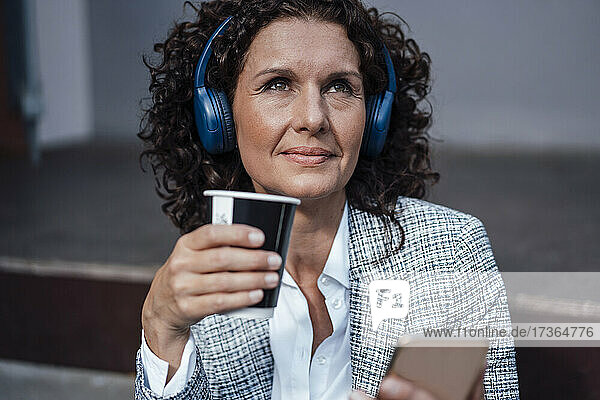Mature businesswoman listening music while holding coffee cup