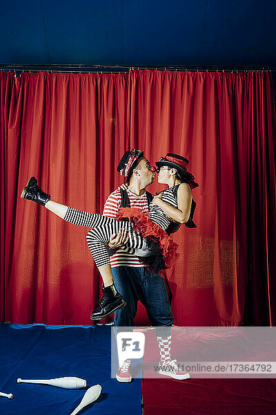 Männlicher und weiblicher Clown küssen sich auf der Zirkusbühne