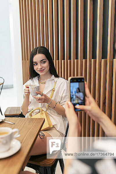 Woman photographing smiling friend through smart phone at food court