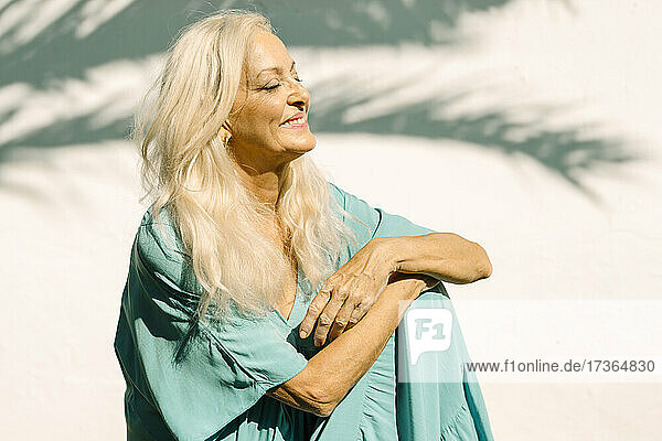 Lächelnde ältere Frau im Ruhestand träumt im Hinterhof an einem sonnigen Tag