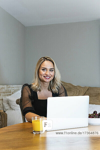 Lächelnde junge Geschäftsfrau mit Laptop im Heimbüro