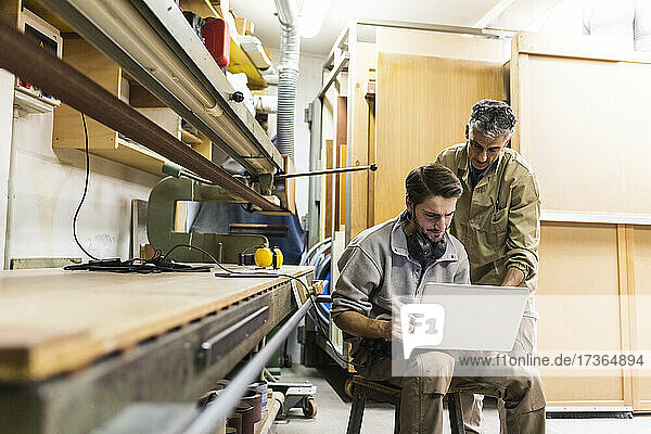 Männliche Kollegen diskutieren am Laptop während der Arbeit in der Werkstatt