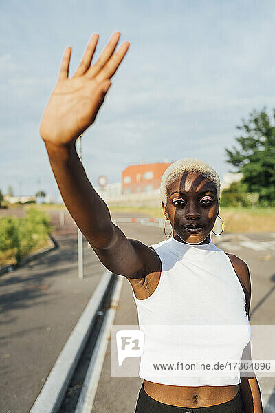 Frau winkt mit der Hand  während sie an einem sonnigen Tag auf der Straße steht