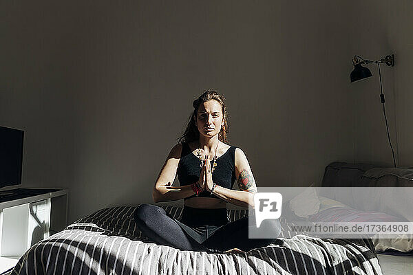 Frau mit verschränkten Händen  die auf dem Bett sitzend Yoga praktiziert