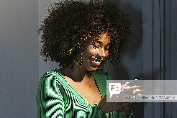 Lächelnde junge Afro-Frau  die zu Hause ein Smartphone benutzt
