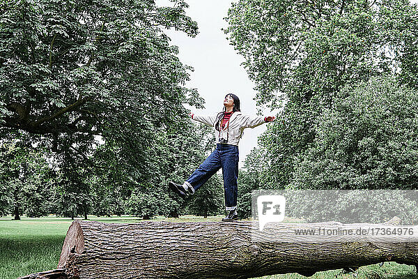 Unbekümmerte junge Frau balanciert auf einem Baumstamm in einem öffentlichen Park