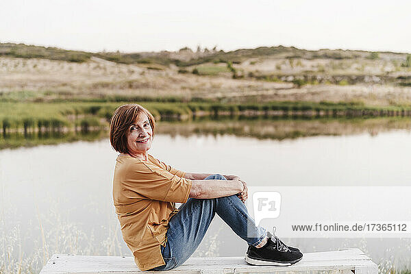 Ältere Frau sitzt auf einer Bank am See