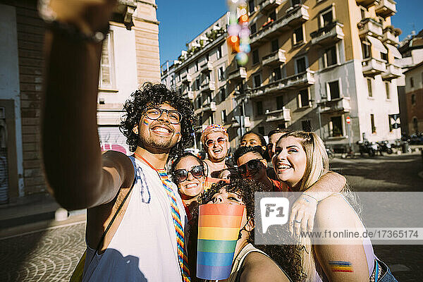 Smiling male and female friends taking selfie on street during sunny day
