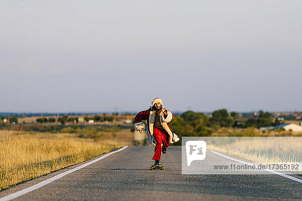 Man wearing Santa Claus costume skateboarding on road during sunset