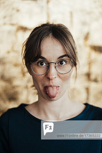 Junge Frau mit Brille streckt die Zunge heraus