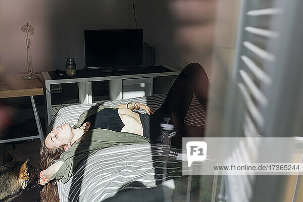Woman relaxing while lying on bed seen through window
