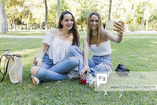 Smiling female friends taking selfie through smart phone at park