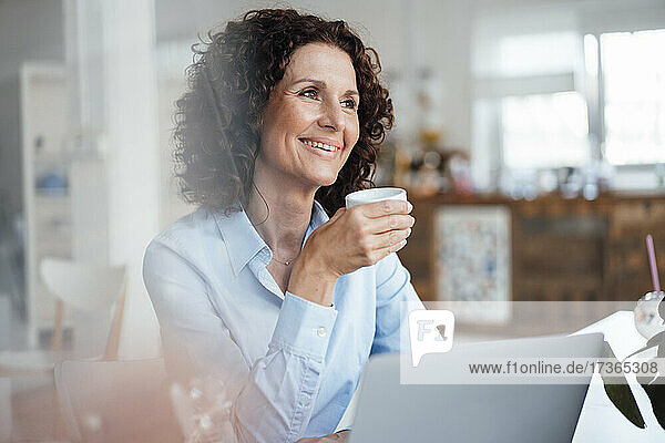 Smiling female professional looking away while having coffee at office