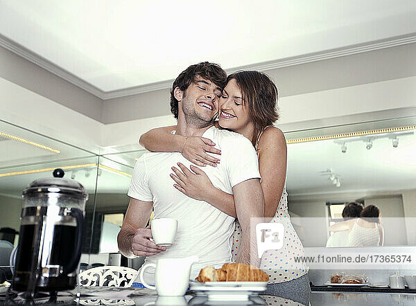 Happy woman embracing boyfriend having coffee at home