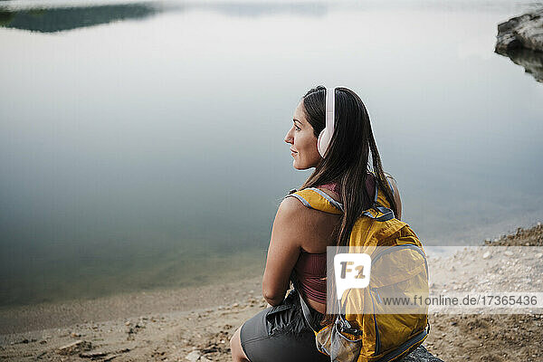 Junge Rucksacktouristin schaut weg  während sie auf einem Felsen am Seeufer sitzt