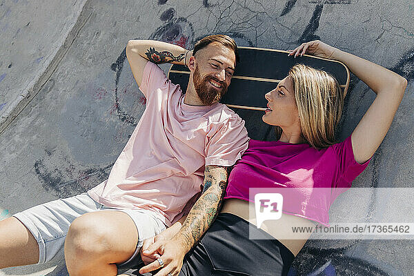 Young couple looking at each other while lying at skateboard park