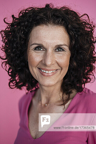 Lockig behaarte Geschäftsfrau lächelnd über rosa Hintergrund