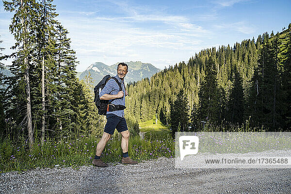 Männlicher Wanderer mit Rucksack  der über die Schulter schaut  während er auf einem unbefestigten Weg geht