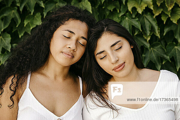 Multiethnische Schwestern mit geschlossenen Augen in der Nähe von Pflanzen
