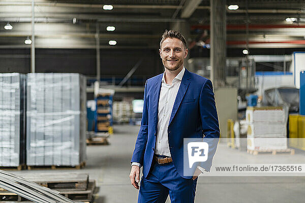 Smiling businessman with hand in pocket standing at industry
