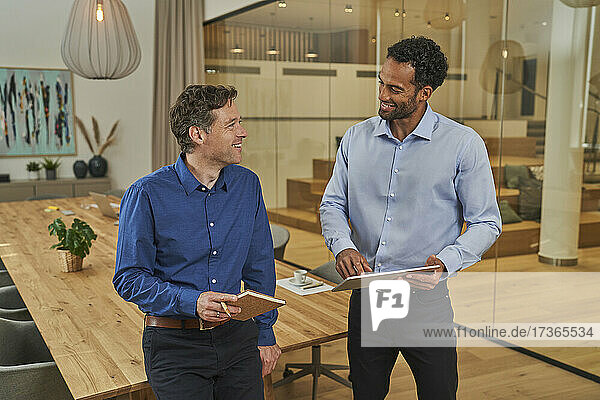 Lächelnde männliche Kollegen  die über ein digitales Tablet im Büro diskutieren