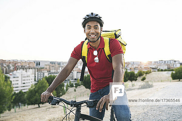 Smiling male delivery person wearing helmet sitting on bicycle