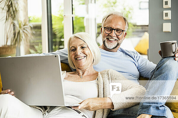 Woman smiling at video call through laptop while sitting with man on sofa