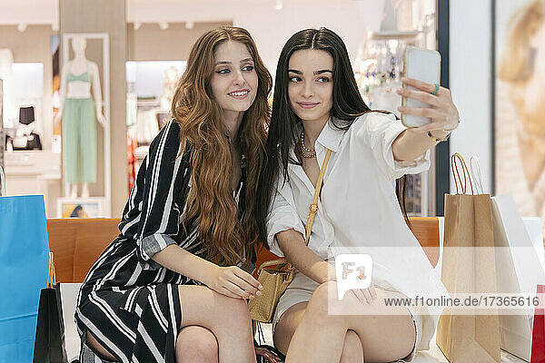 Woman taking selfie with smiling friend through smart phone at mall