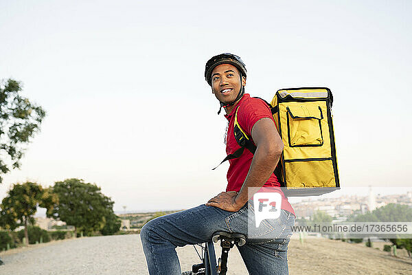 Smiling male delivery person looking away while sitting on bicycle