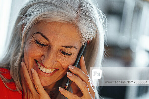 Lächelnde reife Geschäftsfrau  die im Büro mit einem Mobiltelefon spricht