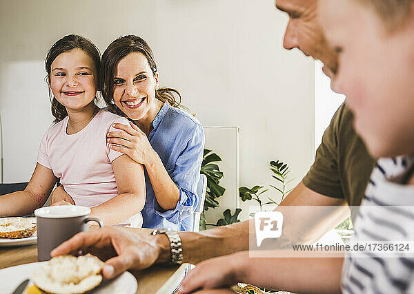 Lächelnde Tochter und Mutter betrachten den Vater beim Frühstück
