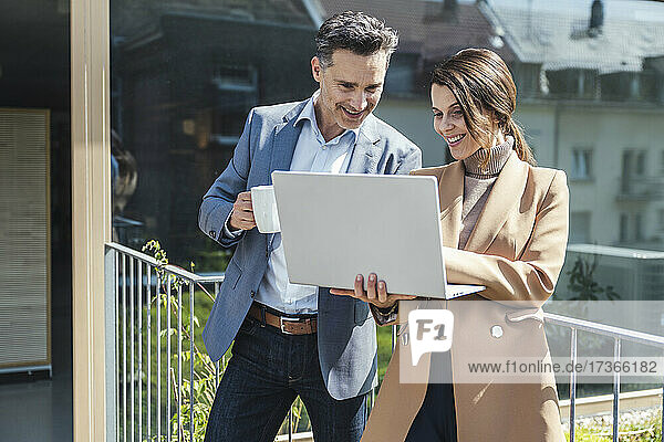 Lächelnde Geschäftsfrau und Geschäftsmann diskutieren am Laptop