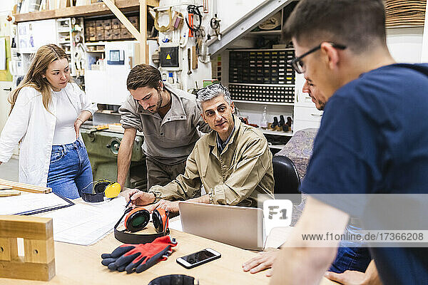 Älterer männlicher Schreiner im Gespräch mit männlichen und weiblichen Kollegen am Tisch in der Werkstatt