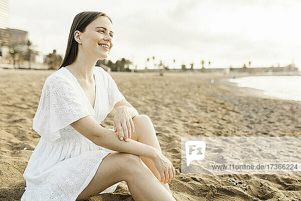 Lächelnde junge Frau am Strand sitzend