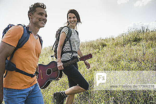 Smiling woman with guitar walking by man on grass