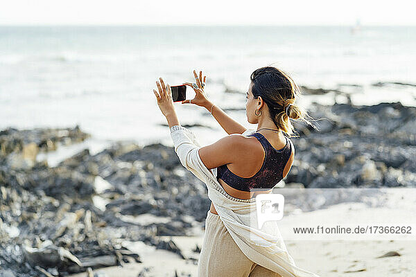 Woman holding smart phone while photographing at beach