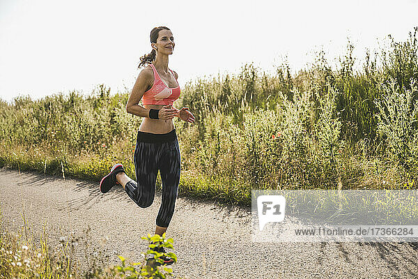 Female athlete with wireless-in ear headphones running on road