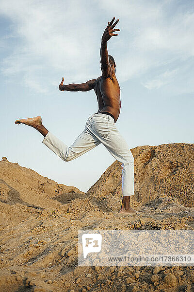 Mann ohne Hemd mit ausgestreckten Armen tanzt auf Sand