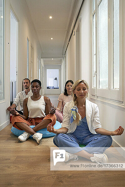 Mid adult coworkers meditating while sitting at corridor