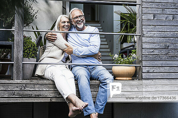 Fröhliches reifes Paar  das sich umarmt  während es auf dem Balkon sitzt