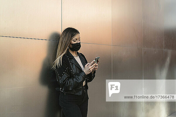 Young woman wearing protective face mask using smart phone during pandemic