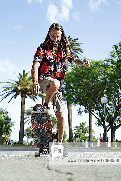 Junger Mann mit langen Haaren fährt auf der Straße Skateboard