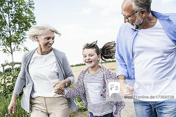 Fröhliches Mädchen hält die Hände der Großeltern beim Laufen im Freien