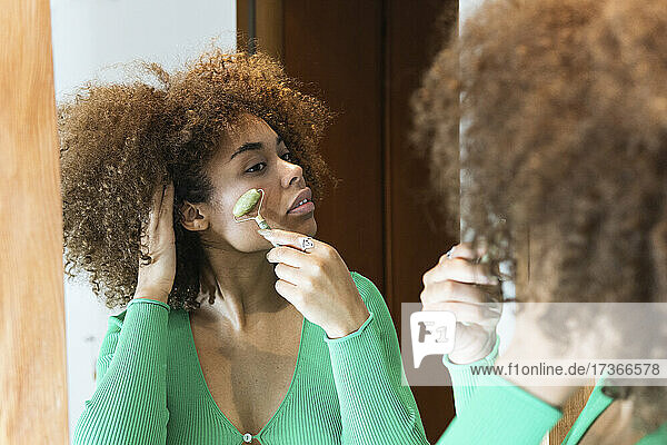 Afro young woman massaging face with jade roller at home