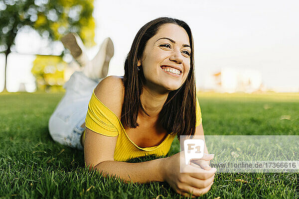 Glückliche junge Frau  die wegschaut  während sie sich im Gras entspannt