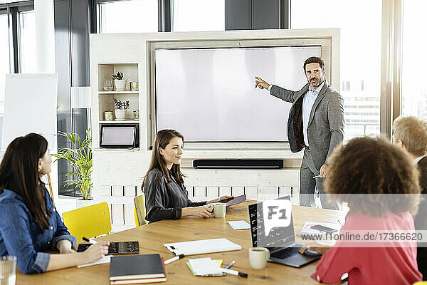 Männlicher Fachmann  der auf die Projektionsfläche zeigt  während er mit einem Kollegen in einer Besprechung arbeitet